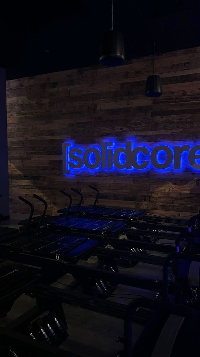 A blue-lit solidcore sign on a wooden wall above rows of reformers.